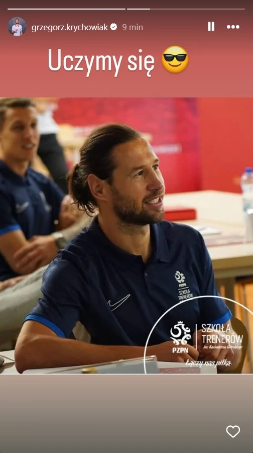 Grzegorz Krychowiak podczas Szkoły Trenerów PZPN Mężczyzna z długimi włosami w niebieskiej koszulce sportowej siedzi przy stole w sali szkoleniowej, skupiony na zajęciach. W tle widoczna jest jeszcze jedna osoba z uśmiechem na twarzy. Na zdjęciu znajduje się logo szkoły trenerów PZPN oraz napis 'Uczy...