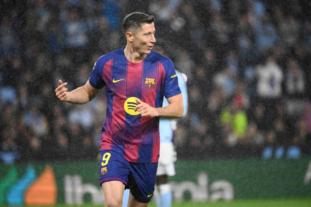 Robert Lewandowski w FC Barcelona Piłkarz ubrany w niebiesko-bordową koszulkę FC Barcelony biegnie po murawie stadionu podczas meczu piłki nożnej w deszczu, w tle widoczni są rozmazani zawodnicy drużyny przeciwnej oraz widownia.