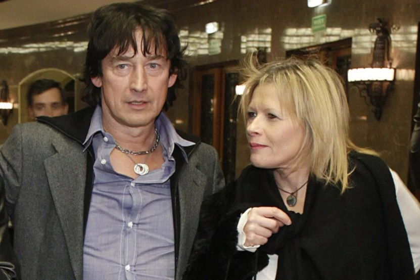 Mężczyzna i kobieta stoją obok siebie w eleganckim otoczeniu, ujęcie skupia się na ich twarzach i sylwetkach, w tle widoczne są światła oraz wnętrze budynku.