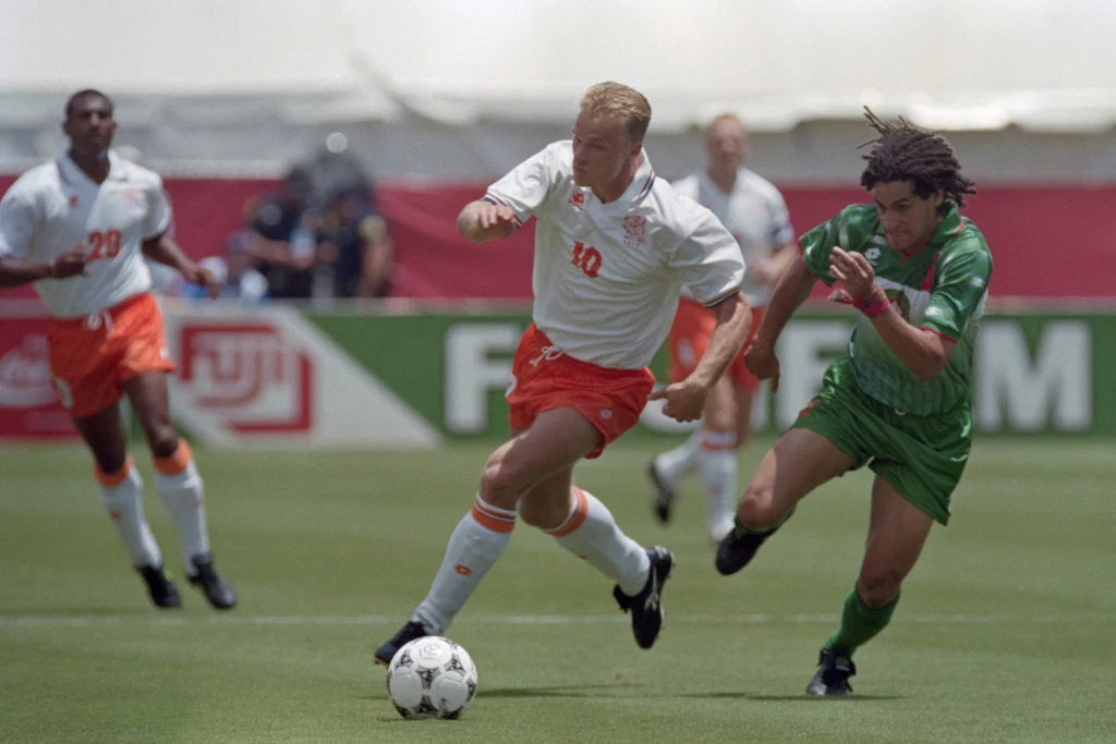 Dennis Bergkamp w Poznaniu okazał się katem Polaków. Jego dublet dał awans na mundial. Holandia w USA dotarła do ćwierćfinału Dwóch piłkarzy walczących o piłkę na boisku, jeden ubrany w biało-pomarańczowy strój, drugi w zielony, w tle widoczni są pozostali zawodnicy i elementy stadionu.