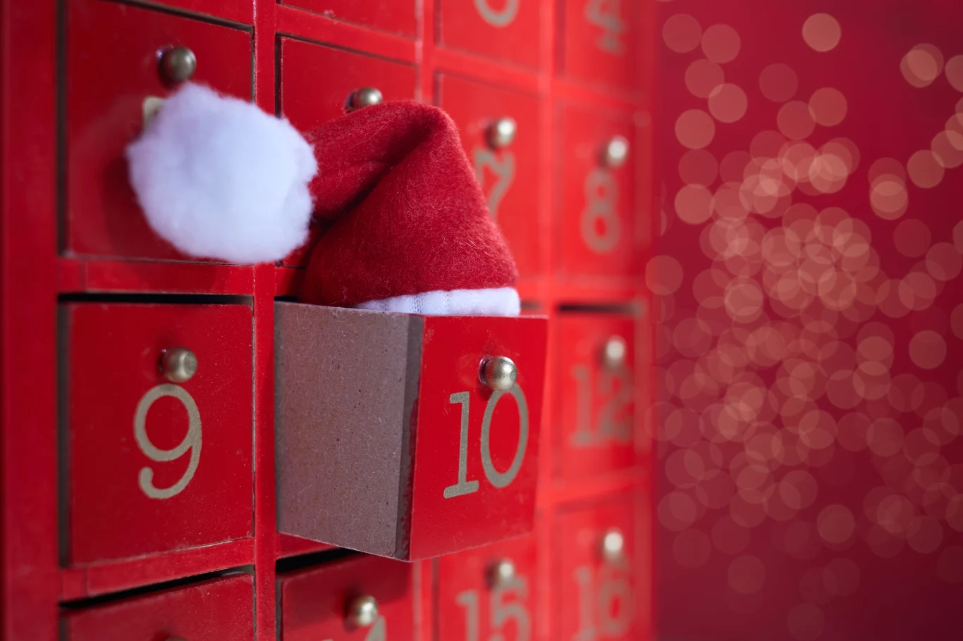 Kalendarze adwentowe: od czekoladek po ekskluzywne gadżety Kalendarz adwentowy z czerwonymi ponumerowanymi szufladkami, z jednej z nich wystaje czapka Mikołaja.