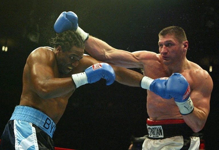 Chris Byrd - Andrzej Gołota. To wtedy Polak był najbliżej mistrzostwa świata Dwóch bokserów w ringu podczas dynamicznego pojedynku, jeden z zawodników zadaje silny cios w głowę przeciwnika, obaj ubrani w rękawice bokserskie i sportowe spodenki, wyraziste emocje walki sportowej.