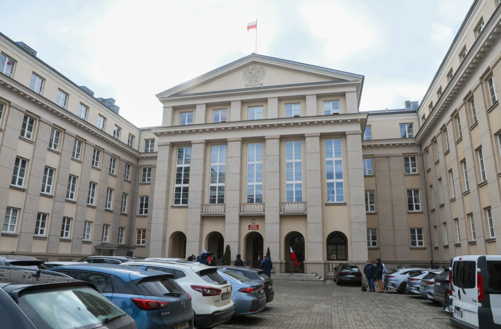 Byłemu prezesowi NIK postawiono prokuratorskie zarzuty Duży budynek urzędowy z flagą Polski na dachu, otoczony zaparkowanymi samochodami; na dziedzińcu przebywa kilka osób, wejście ozdobione polskimi symbolami narodowymi.