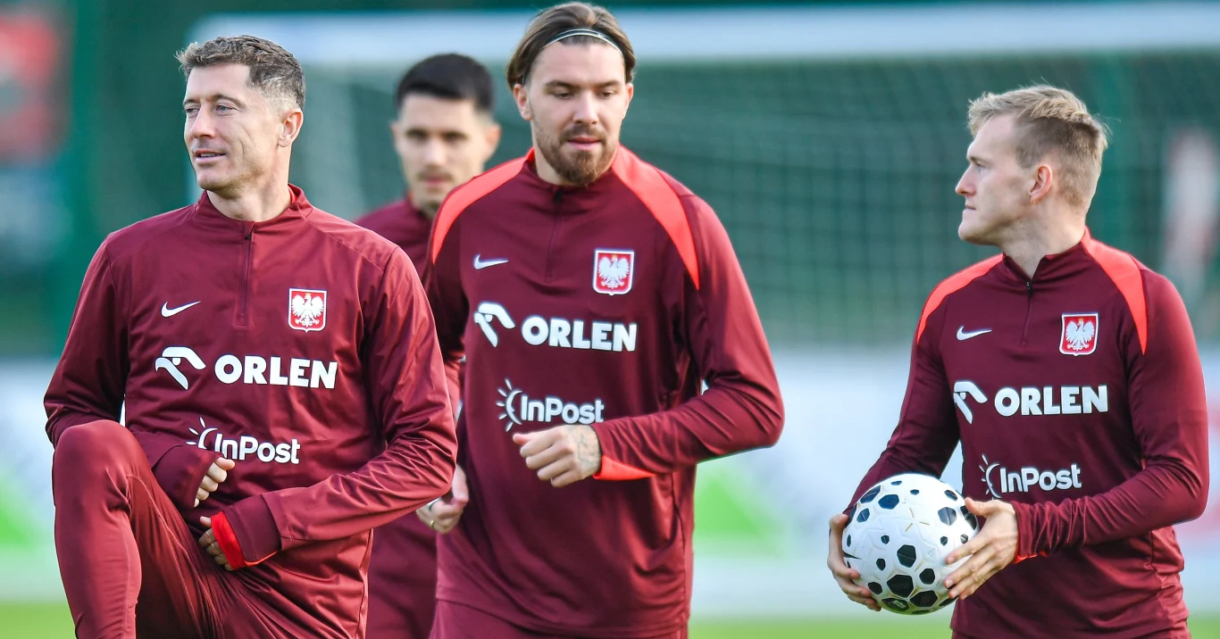 Przemysław Wiśniewski (w środku) w tym tygodniu nie zrzuci treningowego dresu kadry Grupa polskich piłkarzy w bordowych strojach sportowych podczas treningu na murawie, jeden z zawodników trzyma piłkę, pozostali rozmawiają i przygotowują się do ćwiczeń, w tle bramka piłkarska.