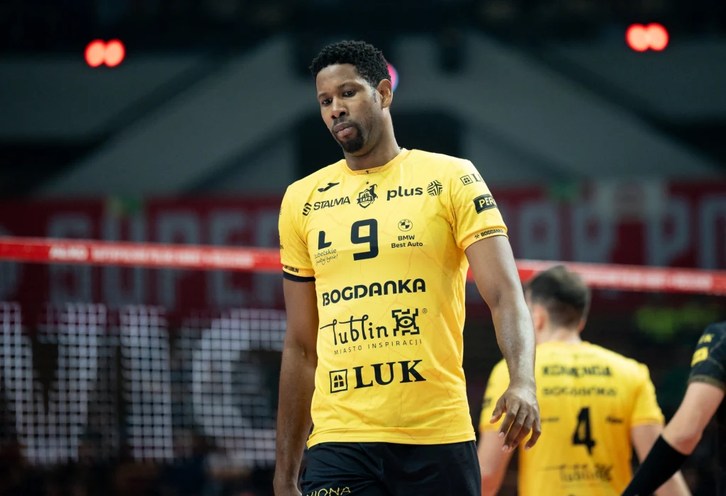 Wilfredo Leon w barwach Bogdanki LUK Lublin Siatkarz w żółtej koszulce z numerem 9 oraz logotypami sponsorów stoi na boisku, w tle widoczny drugi zawodnik z tej samej drużyny oraz elementy hali sportowej.