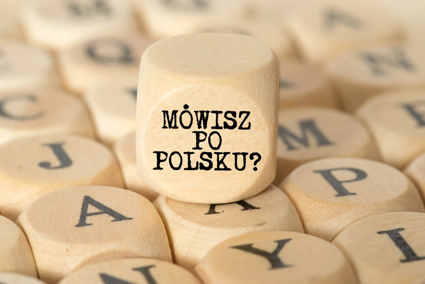 Rozwiąż quiz o najpopularniejszych błędach językowych! Drewniana kostka z napisem 'Mówisz po polsku?' otoczona innymi kostkami z czarnymi literami alfabetu.