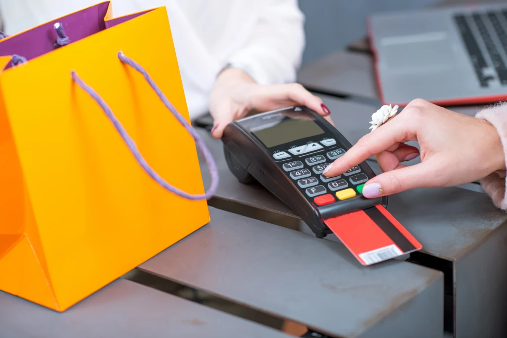 Jeśli uwierzymy, że mamy do czynienia z produktem ekskluzywnym, prędzej pogodzimy się z jego zawyżoną ceną Ręka osoby wprowadza kod PIN na terminalu płatniczym podczas transakcji kartą płatniczą, obok znajduje się pomarańczowa torba na zakupy.