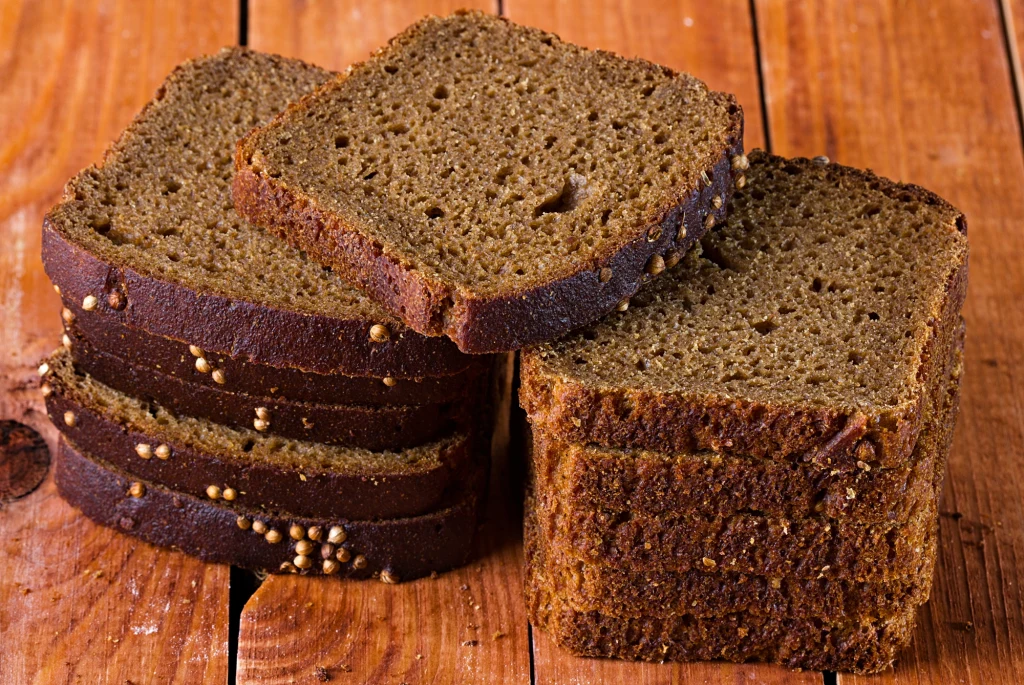 Dobry jakościowo chleb razowy wyróżnia się nie tylko kolorem skórki Kilka kromek świeżego razowego chleba z ziarnami ułożonych na drewnianej powierzchni.
