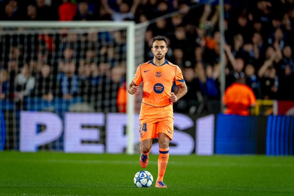 Eric Garcia Piłkarz w pomarańczowym stroju drużyny FC Barcelona prowadzi piłkę po murawie stadionu podczas meczu, w tle widoczni kibice oraz reklama marki Pepsi.