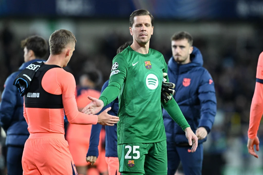 Wojciech Szczęsny Dwóch piłkarzy na boisku, jeden ubrany w zielony strój bramkarski z numerem 25, podaje rękę zawodnikowi przeciwnej drużyny ubranemu w różowy strój sportowy, w tle widać innych graczy i rozmazaną publiczność.