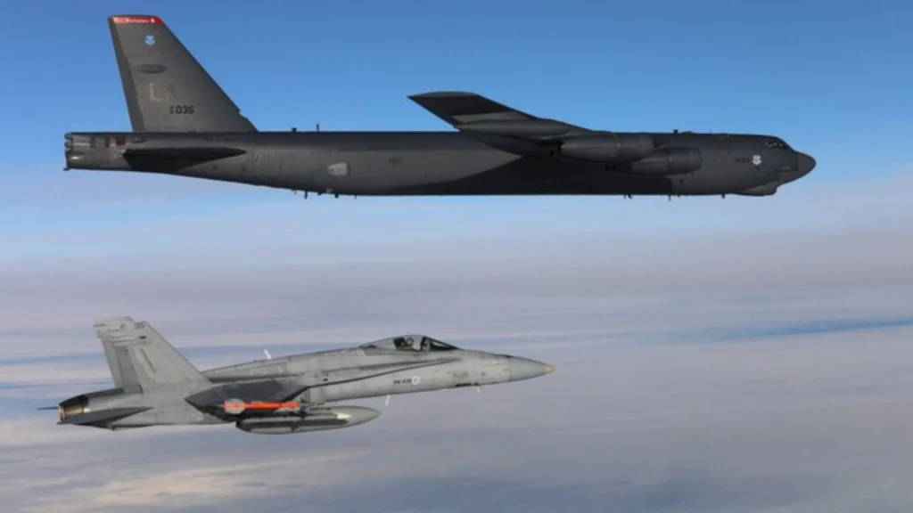 Bombowiec USA B-52H nad Finlandią Dwa wojskowe samoloty lecą obok siebie na tle nieba, większy bombowiec znajduje się wyżej, a myśliwiec nieco niżej.
