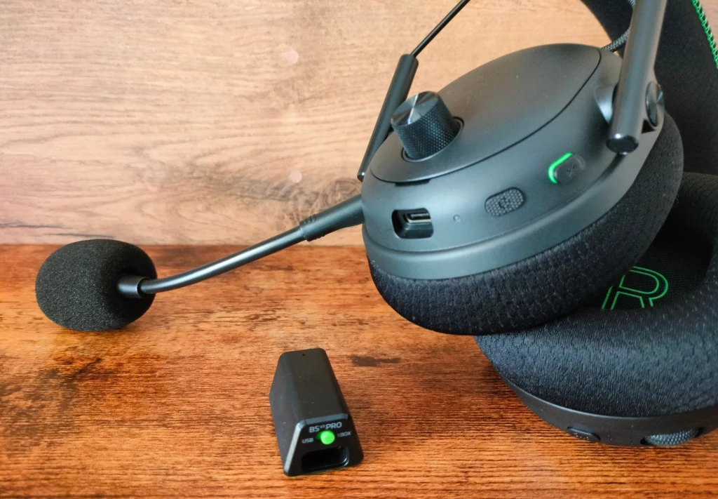 Razer Blackshark V3 Pro Bezprzewodowe słuchawki gamingowe z mikrofonem na wysięgniku, wykonane z czarnego tworzywa, obok znajduje się odbiornik USB. Słuchawki są nowoczesne, z przyciskami i pokrętłem regulacji na nauszniku.