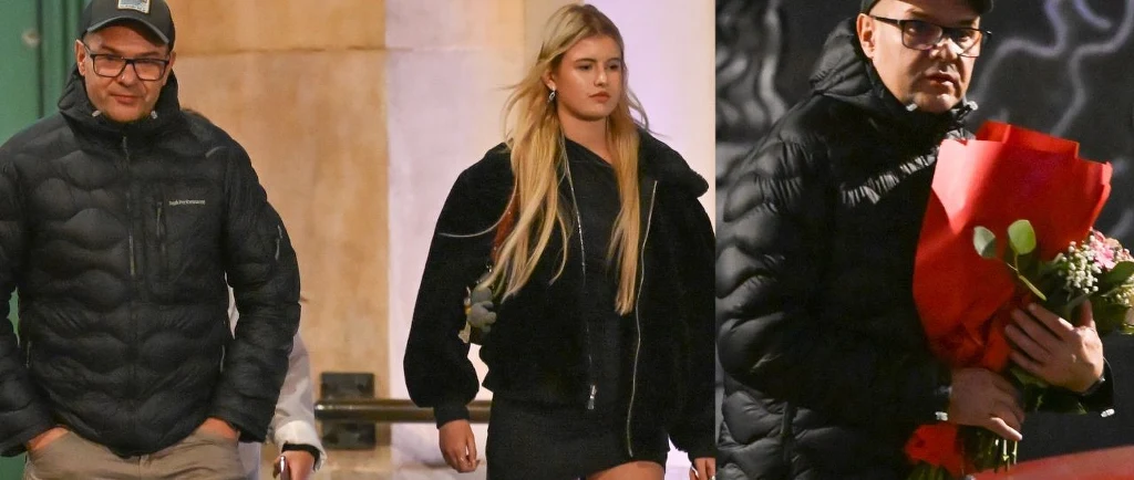 Dwie osoby idące ulicą, mężczyzna ubrany w ciemną kurtkę z czapką oraz młoda kobieta w czarnej kurtce i krótkiej spódnicy, po prawej stronie mężczyzna trzyma bukiet kwiatów owinięty w czerwony papier.