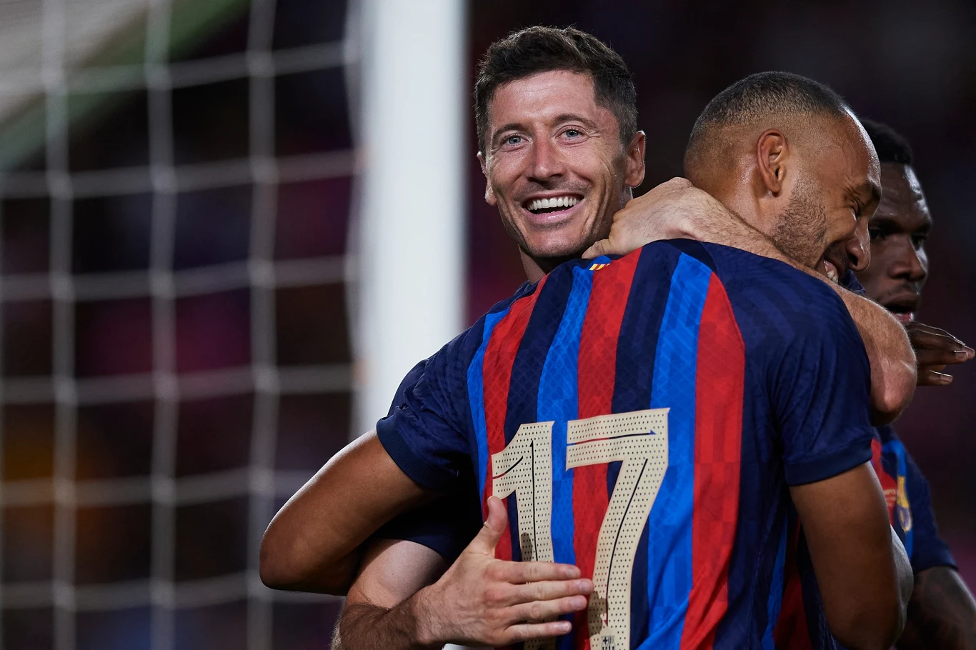 Piłkarze drużyny FC Barcelona świętują zdobycie bramki, jeden z zawodników z numerem 17 zostaje uściskany przez kolegów, jeden z nich uśmiecha się szeroko.