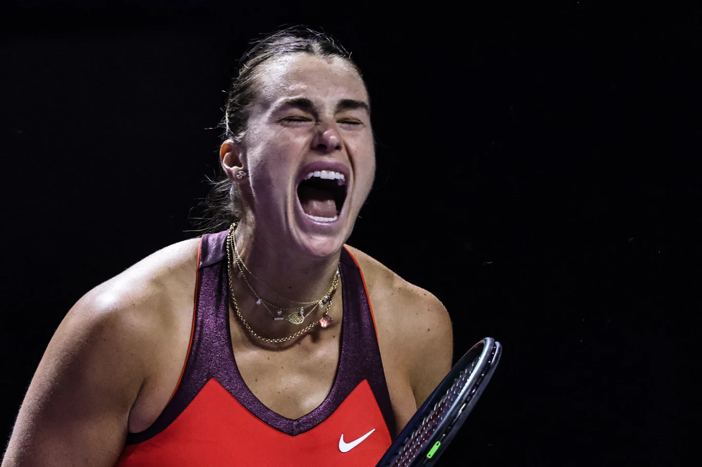Aryna Sabalenka Tenisistka w czerwonym stroju sportowym z wyraźnym wyrazem emocji na twarzy, trzymająca rakietę tenisową. Intensywne światło skupia uwagę na jej ekspresji i sportowej postawie, tło ciemne.