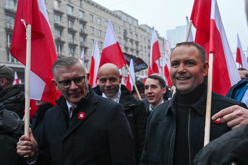 Karol Nawrocki wziął udział w Marszu Niepodległości. Polacy ocenili ten ruch w nowym sondażu Tłum ludzi trzymających polskie flagi maszeruje ulicą miasta, w centrum kilka uśmiechniętych osób, jedna z nich w garniturze, w tle widoczne budynki mieszkalne.
