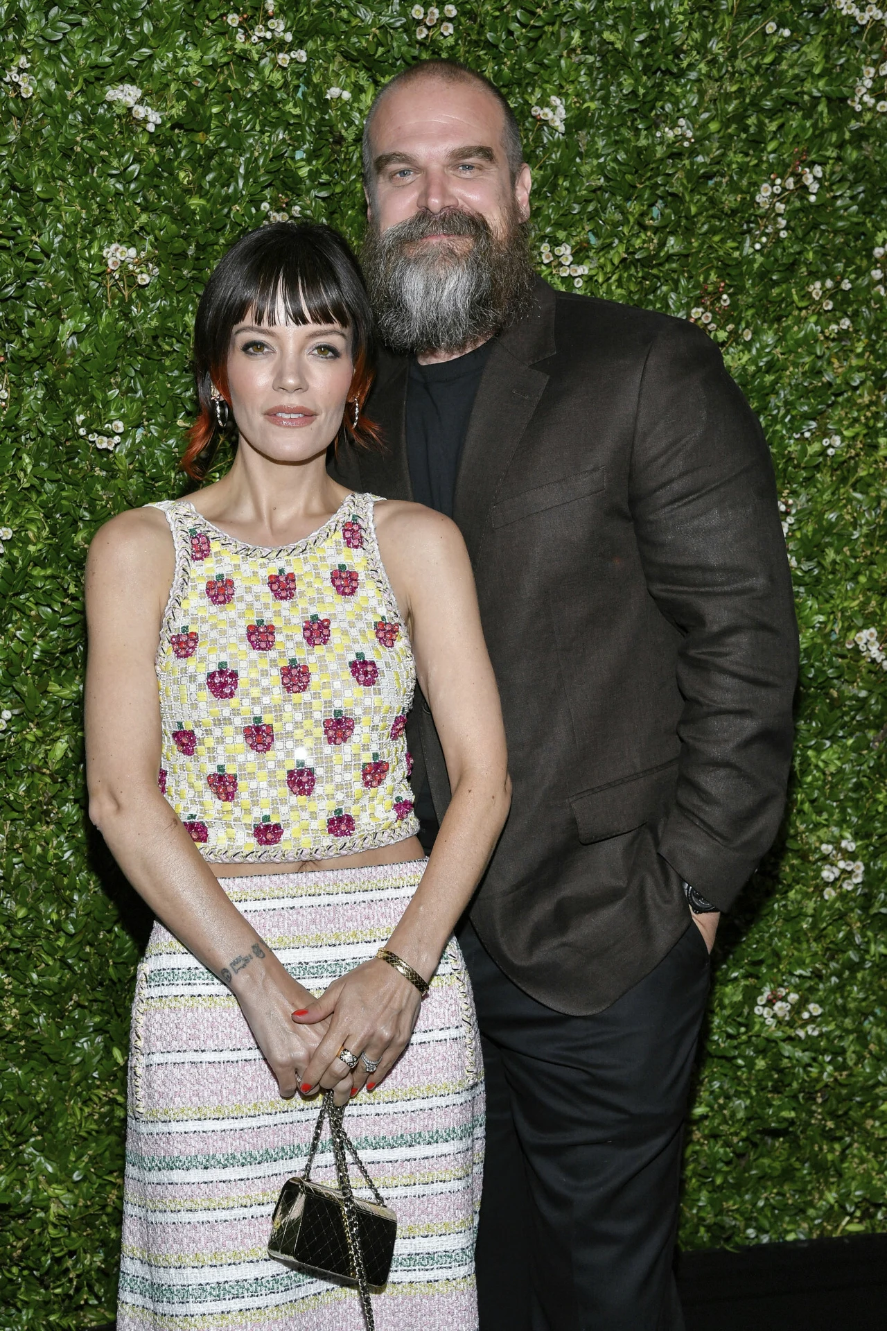 Lily Allen i Davod Harbour byli małżeństwem przez 4 lata Kobieta w jasnej sukience ozdobionej kolorowym wzorem kwiatowym oraz mężczyzna z brodą ubrany w ciemny garnitur stoją razem na tle zielonego żywopłotu.