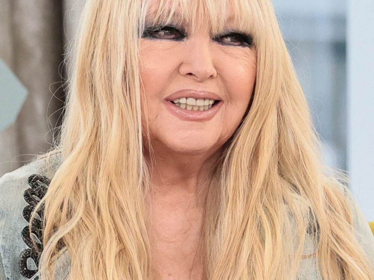 Maryla Rodowicz Kobieta o długich blond włosach i delikatnym makijażu, uśmiechnięta, ubrana w jasną kurtkę z ozdobnym haftem na ramieniu, znajduje się w jasnym wnętrzu.