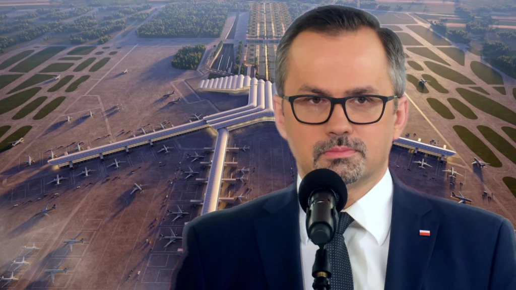 Marcin Horała komentuje sprzedaż działki pod CPK Mężczyzna w garniturze i okularach, stojący przed mikrofonem na tle wizualizacji dużego lotniska z licznymi pasami startowymi i samolotami ustawionymi przy terminalach.
