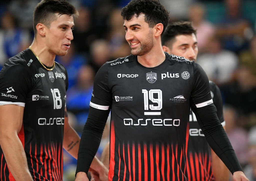 KLemen Cebulj (z lewej) w tym sezonie występuje w Asseco Resovii wspólnie z Marcinem Januszem Siatkarze drużyny Asseco Resovia ubrani w czarne koszulki z czerwonymi akcentami, stoją razem na boisku, jeden z zawodników uśmiecha się.