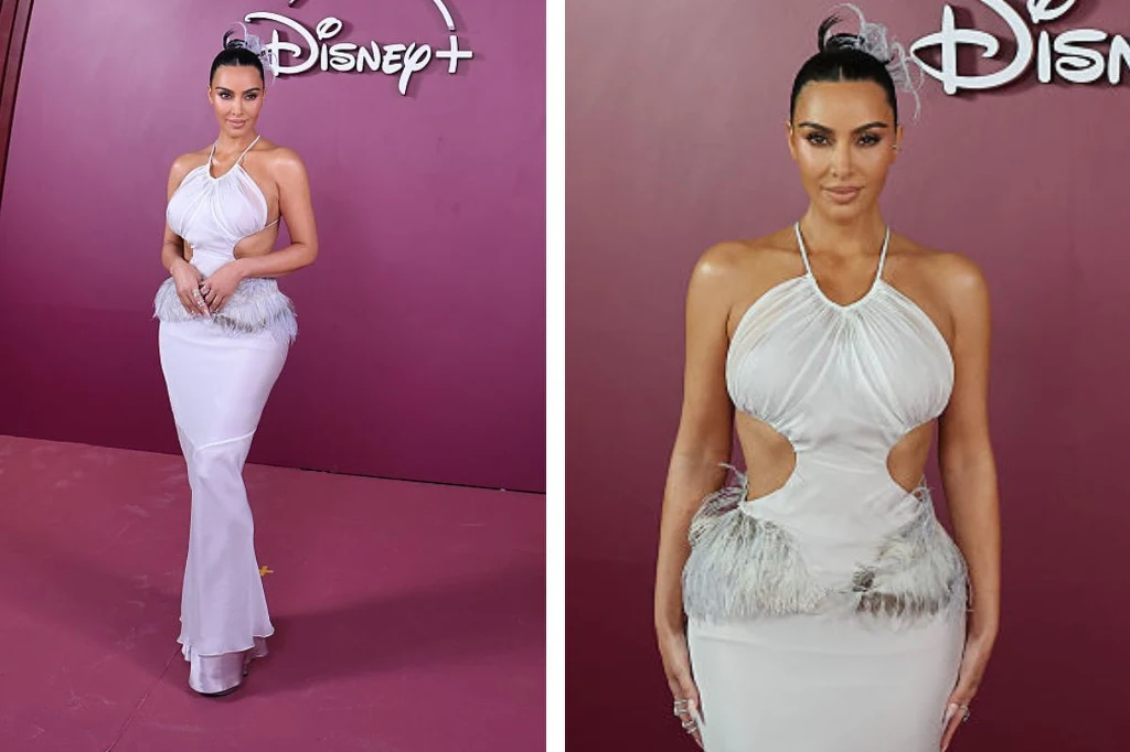 Kreacja Kim Kardashian w Rio de Janerio Kobieta w eleganckiej, białej sukni z wycięciami stoi na tle fioletowej ścianki z logo Disney+. Ma spięte włosy i pewną postawę, prezentując modny strój wieczorowy.