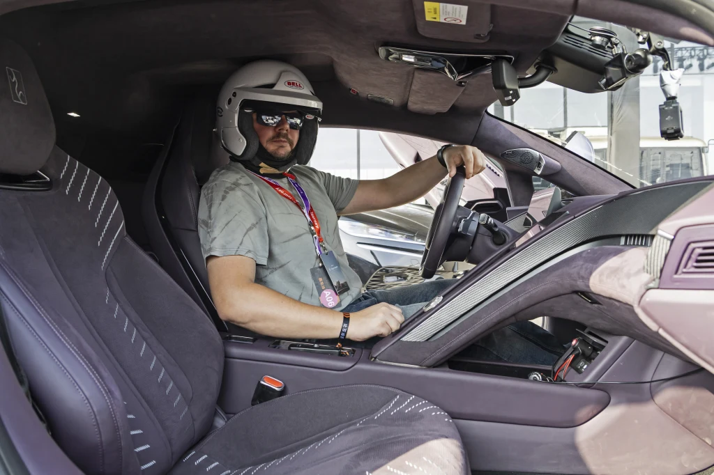 Yangwang U9 nie ma ciasnego wnętrza, ale mając ponad 180 cm wzrostu nie usiądziecie tu wygodnie w kasku Mężczyzna w kasku ochronnym i okularach przeciwsłonecznych siedzi za kierownicą luksusowego samochodu sportowego, trzyma ręce na kierownicy, we wnętrzu pojazdu widoczne zaawansowane wyposażenie oraz tapicerka.