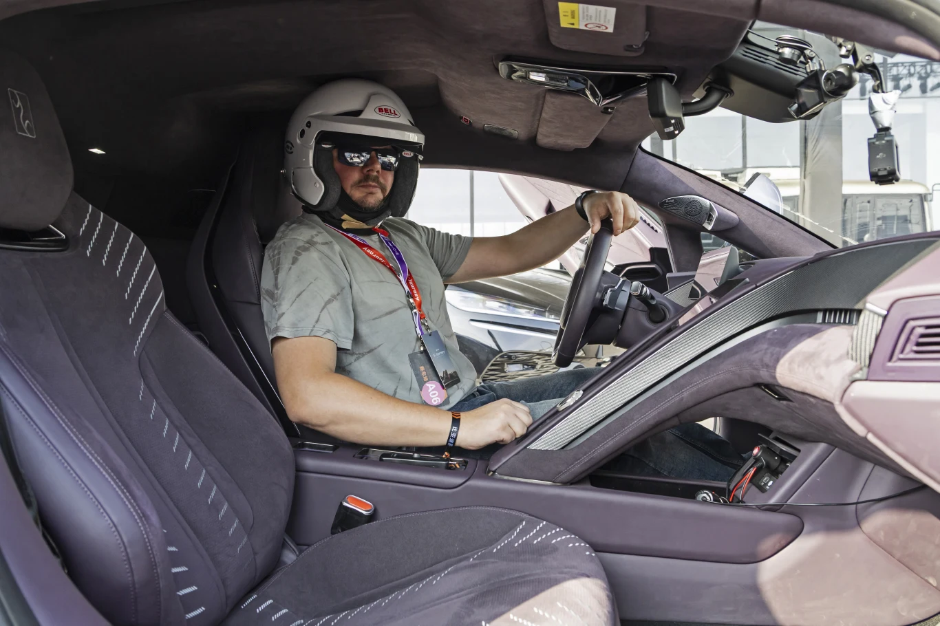 Yangwang U9 nie ma ciasnego wnętrza, ale mając ponad 180 cm wzrostu nie usiądziecie tu wygodnie w kasku Mężczyzna w kasku ochronnym i okularach przeciwsłonecznych siedzi za kierownicą luksusowego samochodu sportowego, trzyma ręce na kierownicy, we wnętrzu pojazdu widoczne zaawansowane wyposażenie oraz tapicerka.