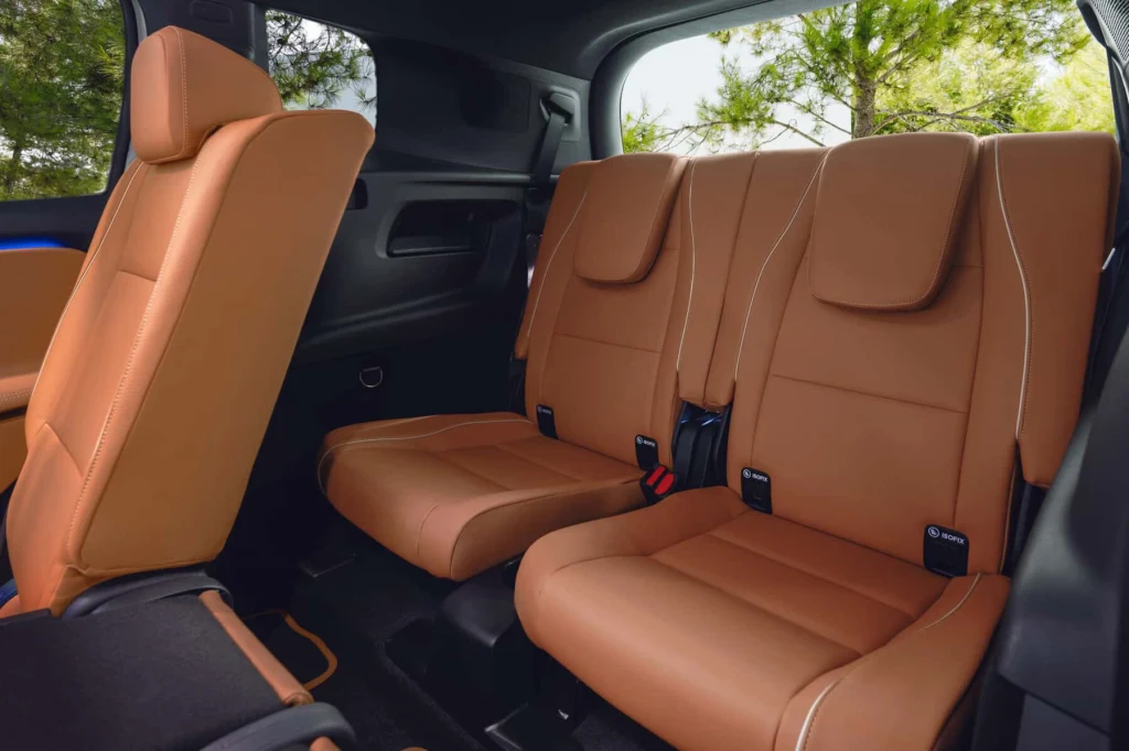 Wnętrze pomieści do siedmiu osób Brązowe, skórzane siedzenia w trzecim rzędzie samochodu osobowego, z widokiem na drzewa przez boczne okno, nowoczesne wykończenie i komfortowe zagłówki.