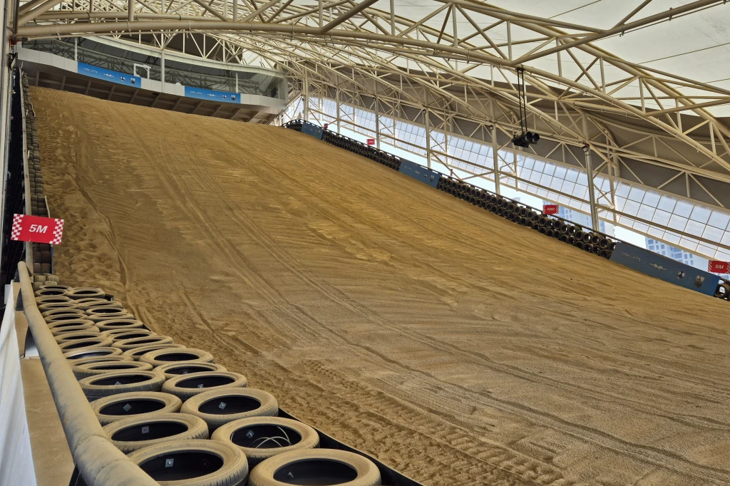 Zdjęcie tego nie oddaje, ale zbocze ma nachylenie 28 stopni i na żywo jest naprawdę strome Stroma, kryta rampa wykonana z ubitej ziemi, otoczona solidną konstrukcją stalową z siatką oświetleń, barierami zabezpieczającymi oraz rzędami opon amortyzujących po bokach. Tabliczka oznaczająca wysokość 5 metrów.