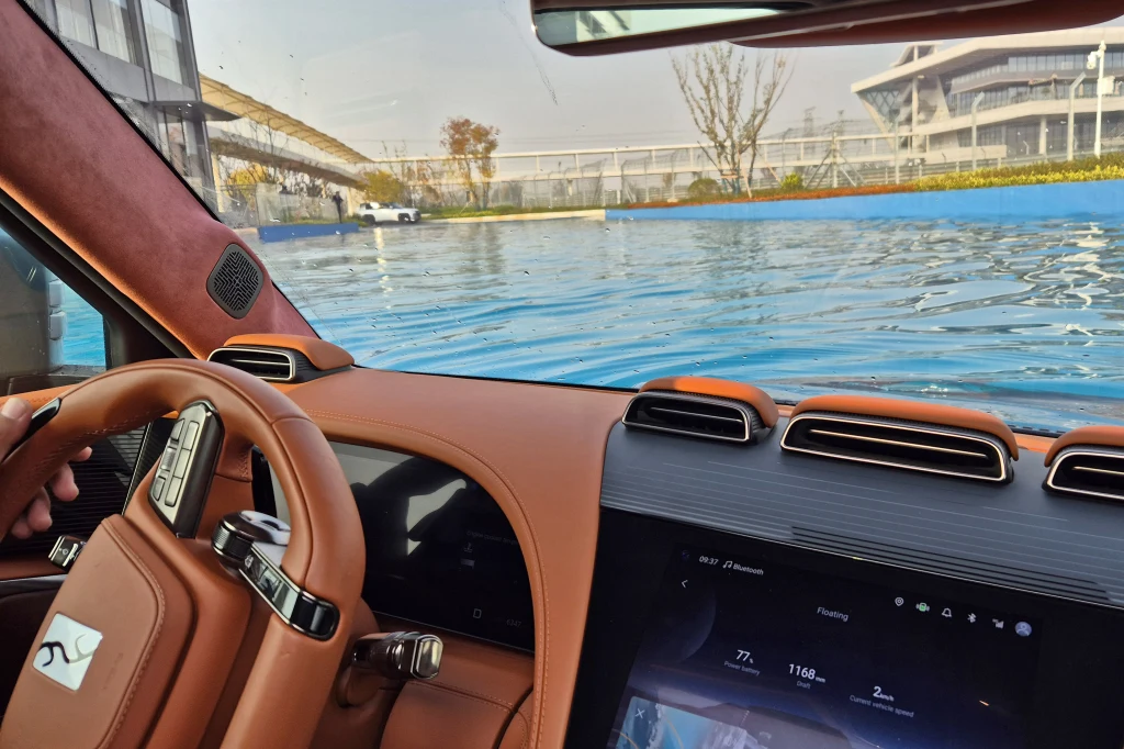 Z perspektywy kierowcy cały przód U8 znajduje się pod wodą Luksusowe wnętrze samochodu z brązową tapicerką, widok na nowoczesny panel sterowania oraz zestaw wskaźników. Przez przednią szybę widać wodę sięgającą niemal do poziomu okien pojazdu, co sugeruje sytuację zalania lub jazdę przez wodę.