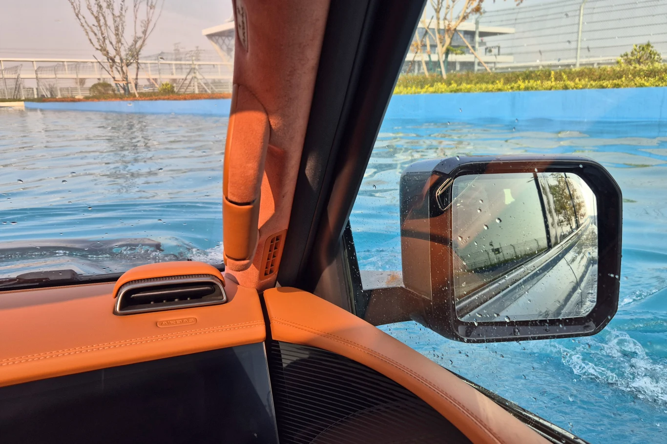 Yangwang U8 Wnętrze samochodu z widokiem przez okno na wodę zalewającą drogę, w lusterku bocznym odbijają się fale oraz fragmenty pojazdu.