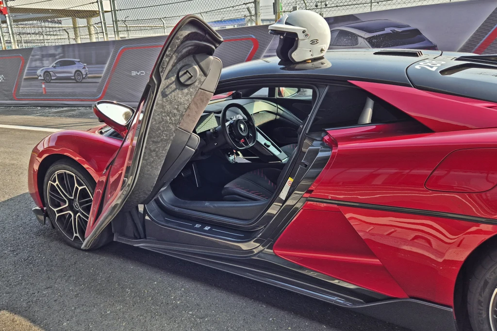 Jak na hipersamochód przystało, drzwi w U9 unoszą się do góry Czerwony supersamochód z unoszonymi do góry drzwiami, sportowym wnętrzem i kaskiem wyścigowym położonym na dachu zaparkowany w pobliżu toru wyścigowego.