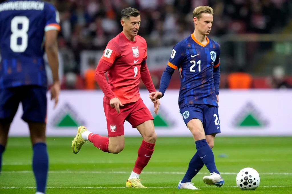 Robert Lewandowski i Frenkie de Jong, 15.11.2025 r. Dwóch piłkarzy rywalizuje ze sobą podczas meczu, jeden w czerwonym stroju z numerem 9, drugi w niebieskim z numerem 21, piłka znajduje się blisko stopy zawodnika w niebieskim stroju, w tle widoczni są inni zawodnicy oraz publiczność na trybunach.