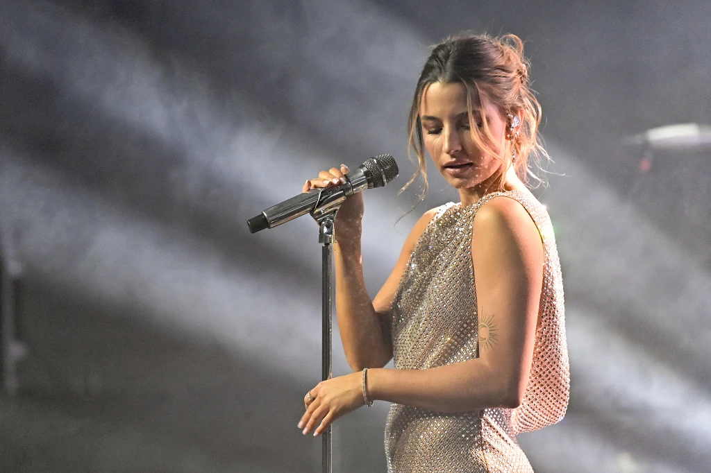 Julia Wieniawa wypoczywa w Meksyku po trasie koncertowej Artystka trzyma mikrofon podczas występu muzycznego, ubrana w lśniącą suknię, z lekko pochyloną głową, w tle widoczne światła sceniczne.