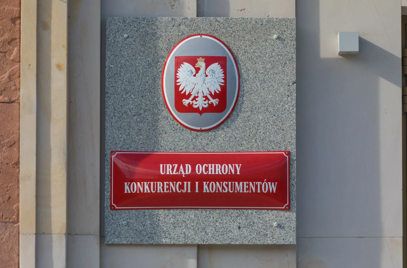 Nawet 2500 zł dla klientów. Znany bank wypłaci odszkodowania Tablica urzędowa Urzędu Ochrony Konkurencji i Konsumentów z godłem Polski umieszczona na zewnętrznej ścianie budynku administracyjnego.