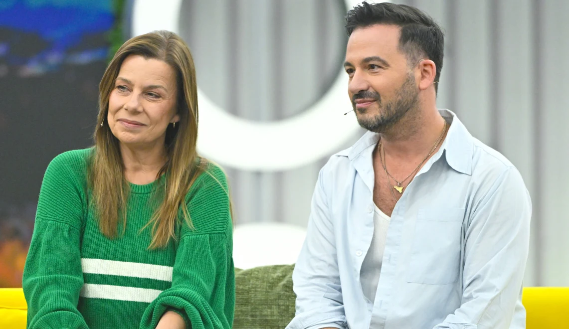 Agata Kulesza, Stefano Terrazzino Dwoje uśmiechniętych ludzi siedzi obok siebie na żółtej kanapie w jasnym wnętrzu. Kobieta ubrana jest w zielony sweter w białe paski, a mężczyzna w jasnoniebieską koszulę oraz biały podkoszulek. Ich wyraz twarzy jest pogodny, a atmosfera wydaje się swo...