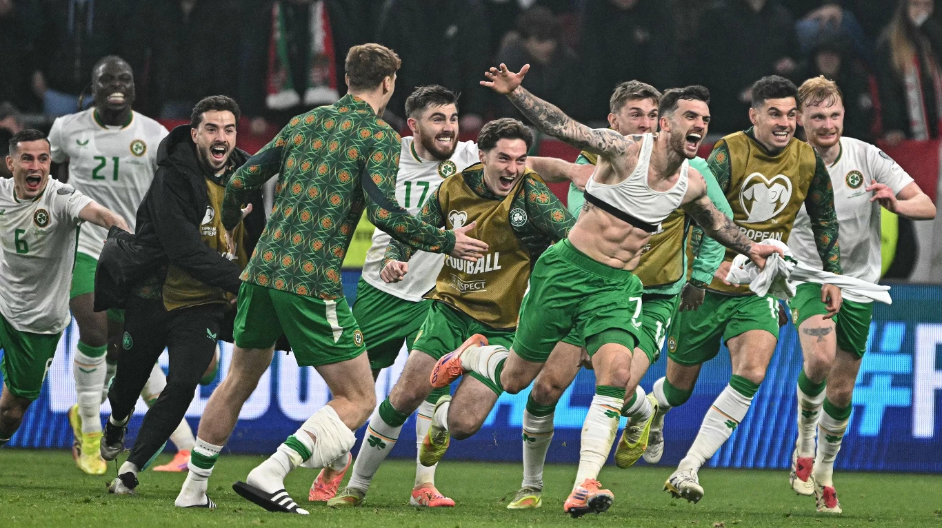 Troy Parrott (bez koszulki) bohaterem narodowym Irlandii Podekscytowani piłkarze w zielonych i białych strojach biegną po murawie, niektórzy ze szczęścia unieśli ręce, a jeden z zawodników zdziera z siebie koszulkę, w tle widoczni kibice i stadionowe światła.