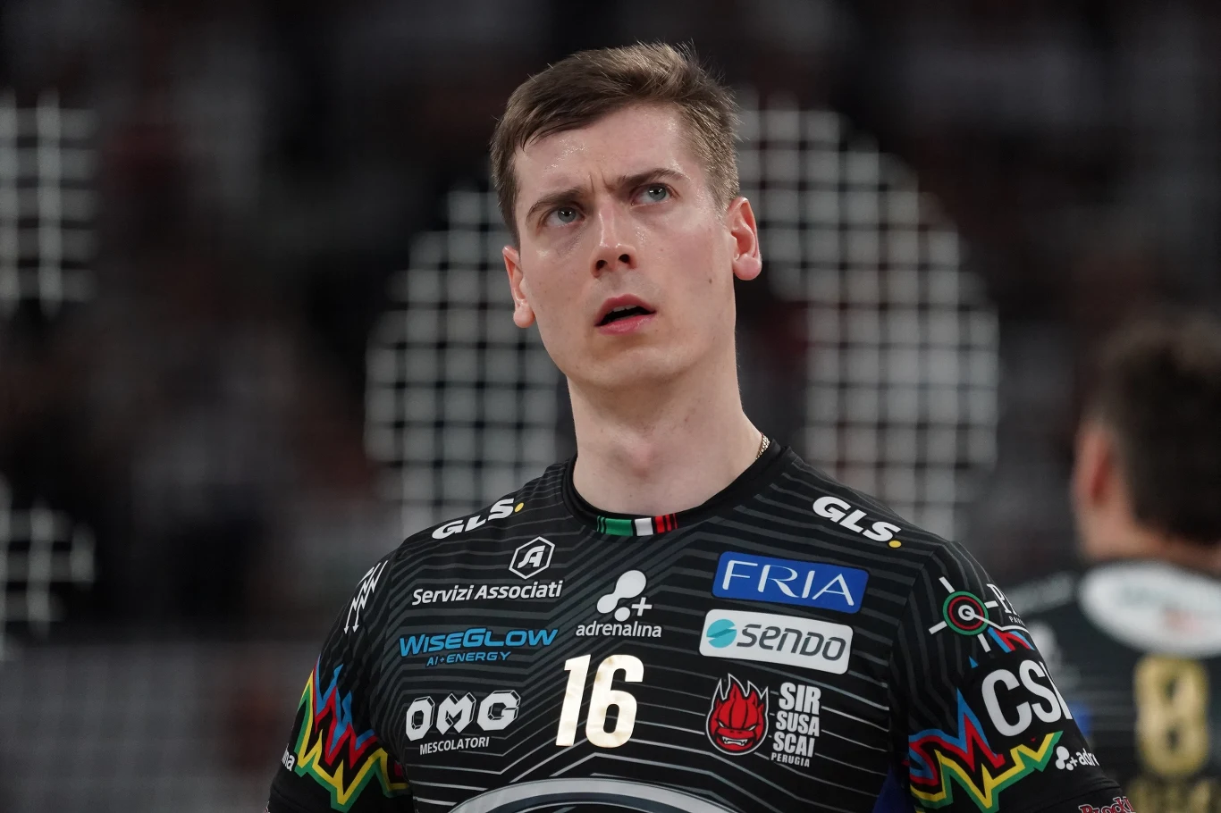 Kamil Semeniuk Siatkarz w czarnej koszulce z numerem 16 stojący na boisku podczas meczu, wokół rozmyta publiczność i siatka.