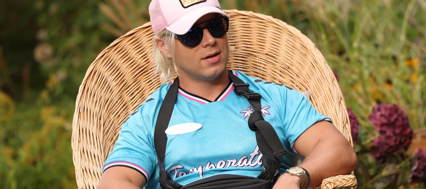 Na posesję Skolima wtargnęło trzech mężczyzn Mężczyzna w jasnoniebieskiej koszulce sportowej, różowej czapce z daszkiem i okularach przeciwsłonecznych siedzi w wiklinowym fotelu na tle roślin ogrodowych. Ma założony temblak na prawą rękę.