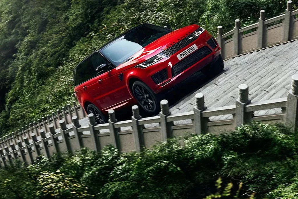W 2018 r. Range Rover Sport dał radę pokonać 999 stopni prowadzących na szczyt Czerwony SUV marki Range Rover pokonuje kamienistą, stromą drogę na tle bujnej, zielonej roślinności oraz tradycyjnych, kamiennych barierek.