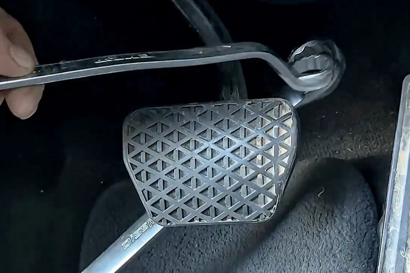 Dwa klucze i kłódka. Złodzieje nie dadzą rady? Screen: dian_arifiya @X Pedał hamulca samochodowego sfotografowany z bliska, przy którym znajduje się metalowy klucz płaski, podłoga wyłożona czarną wykładziną samochodową.