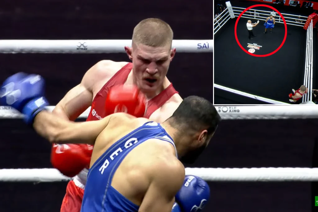 Dwóch bokserów walczy w ringu, jeden z nich w czerwonym stroju zadaje cios przeciwnikowi w niebieskiej koszulce. W tle na górze znajduje się małe okienko z widokiem z góry na ring, na którym widoczni są zawodnicy oraz sędzia.