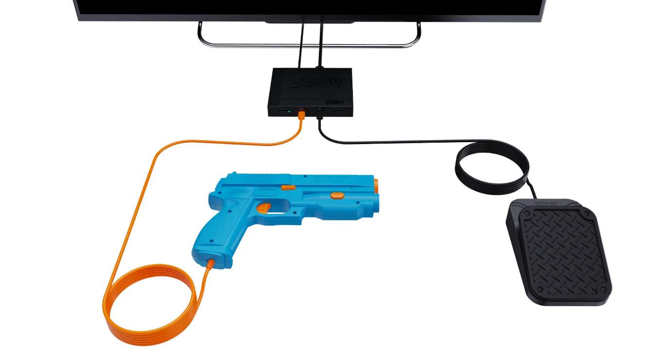 Plastikowy pistolet w kolorze niebieskim z pomarańczowym przewodem, podłączony do czarnego urządzenia oraz pedału, całość leży na jasnym tle i jest elementem elektronicznej gry lub symulatora.