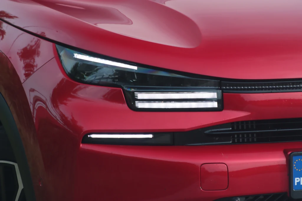 Światła, wszędzie świetła... Czerwony przód nowoczesnego samochodu z wyrazistymi, poziomymi światłami LED i fragmentem europejskiej tablicy rejestracyjnej