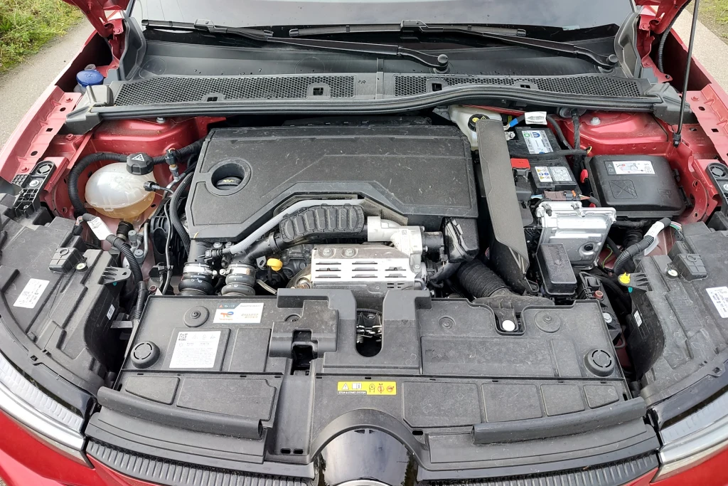 Hybrydowy napęd najpierw miał mieć moc 136 KM. Obecnie wszystkie marki Stellantisa podają, że moc to 145 KM Komora silnika samochodu osobowego z widocznymi elementami takimi jak silnik, akumulator, zbiornik płynu chłodniczego oraz osłony techniczne. Elementy są czyste i wyraźnie oznaczone.