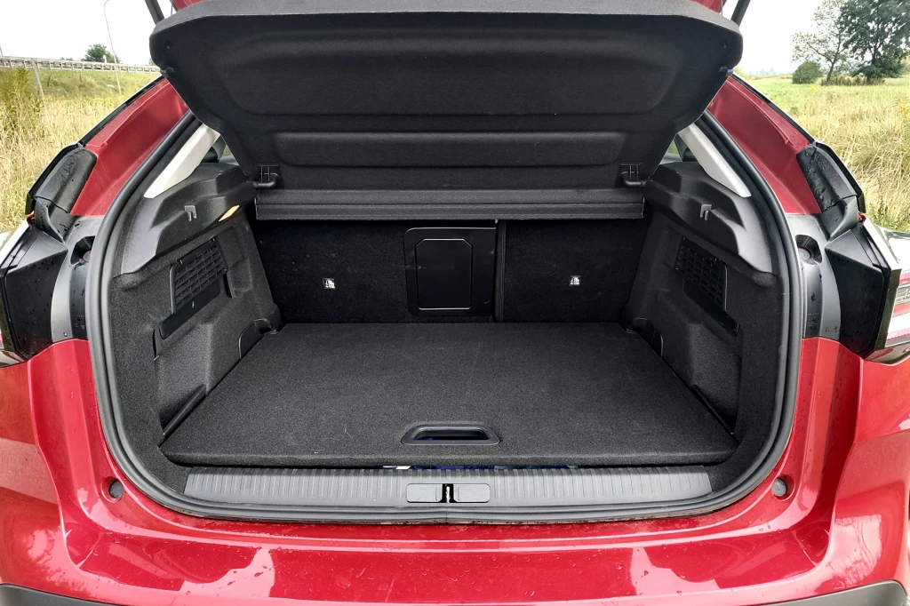 Bagażnik Citroena C4 ma podwójną podłogę, ale tylko 380 litrów pojemności Czerwony samochód z otwartym bagażnikiem o przestronnym wnętrzu, z widocznymi bocznymi schowkami oraz składanym oparciem tylnego siedzenia umożliwiającym powiększenie przestrzeni ładunkowej.