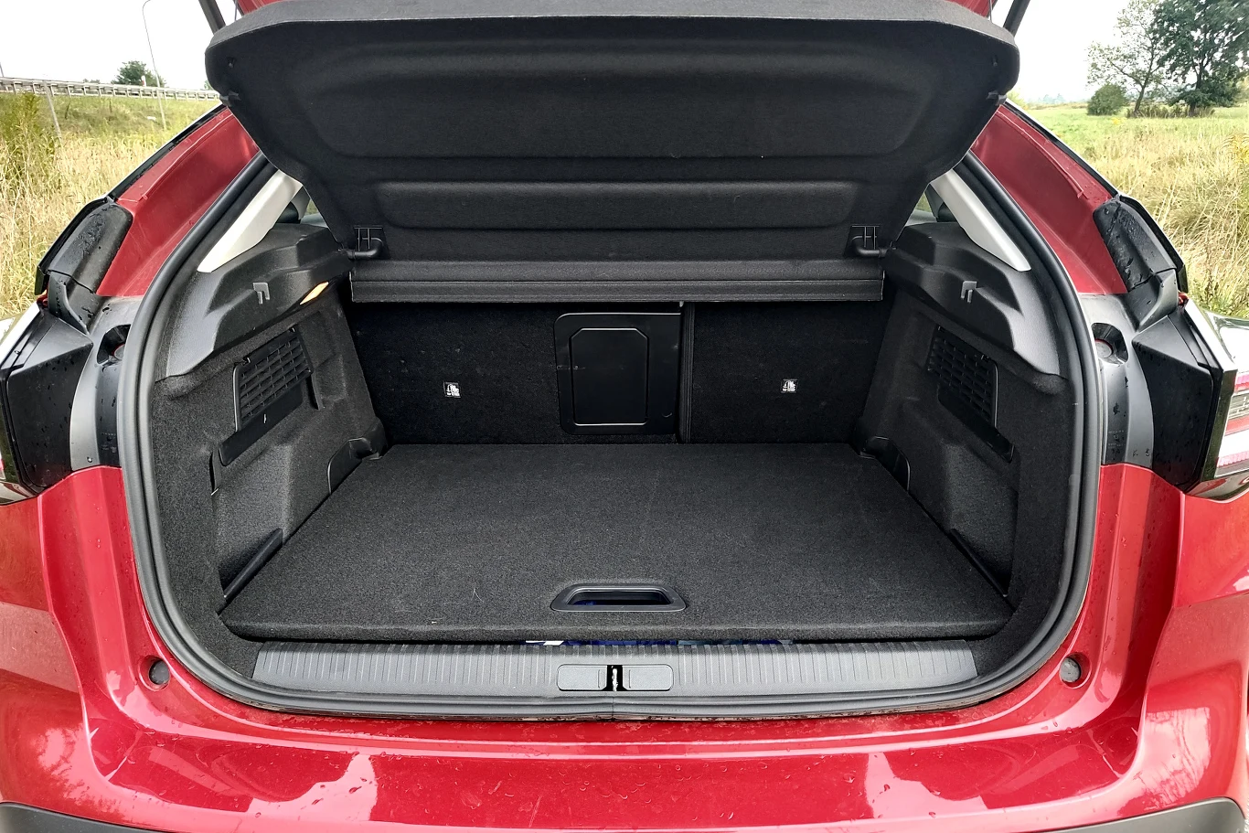 Bagażnik Citroena C4 ma podwójną podłogę, ale tylko 380 litrów pojemności Czerwony samochód z otwartym bagażnikiem o przestronnym wnętrzu, z widocznymi bocznymi schowkami oraz składanym oparciem tylnego siedzenia umożliwiającym powiększenie przestrzeni ładunkowej.