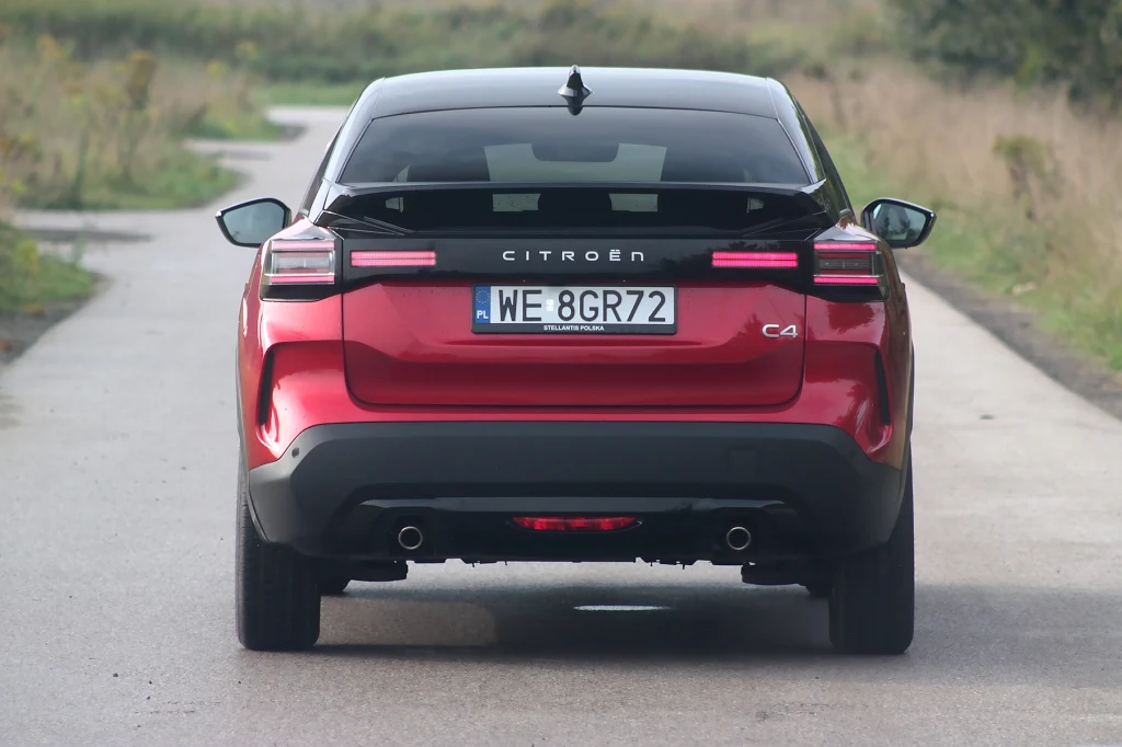 Citroen C4 po liftingu Czerwony samochód Citroën C4 widziany od tyłu, stojący na wąskiej, asfaltowej drodze otoczonej roślinnością. Wyraźnie widoczna tablica rejestracyjna oraz charakterystyczne reflektory tylne.