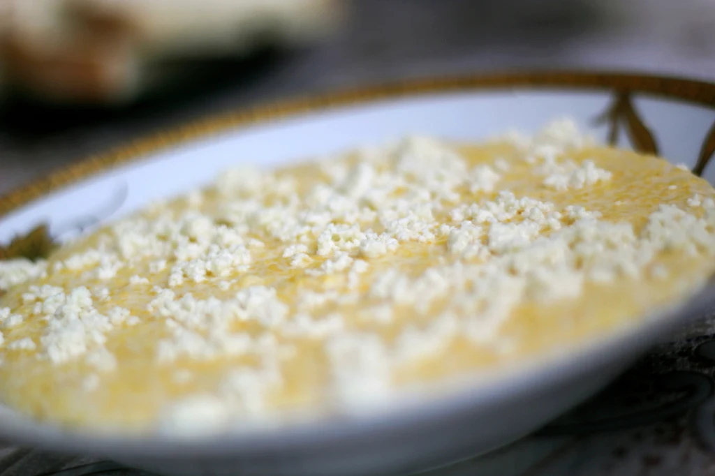 Bryndza jest nafaszerowana probiotykami, które są idealne dla jelit Talerz z żółtym daniem posypanym białym serem, prawdopodobnie kasza lub polenta w połączeniu z twarogiem, widoczne w zbliżeniu