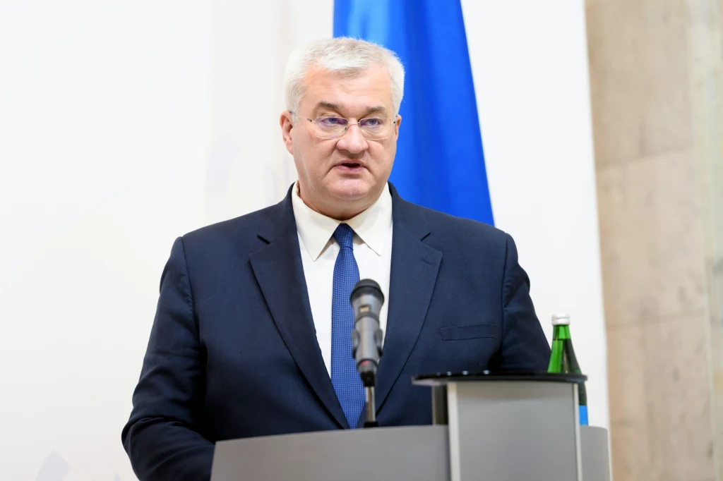 Szef MSZ Ukrainy Andrij Sybiha (zdj. ilustracyjne) Mężczyzna w garniturze i krawacie przemawia przy mównicy, w tle widoczna niebieska flaga oraz butelka wody mineralnej na mównicy.